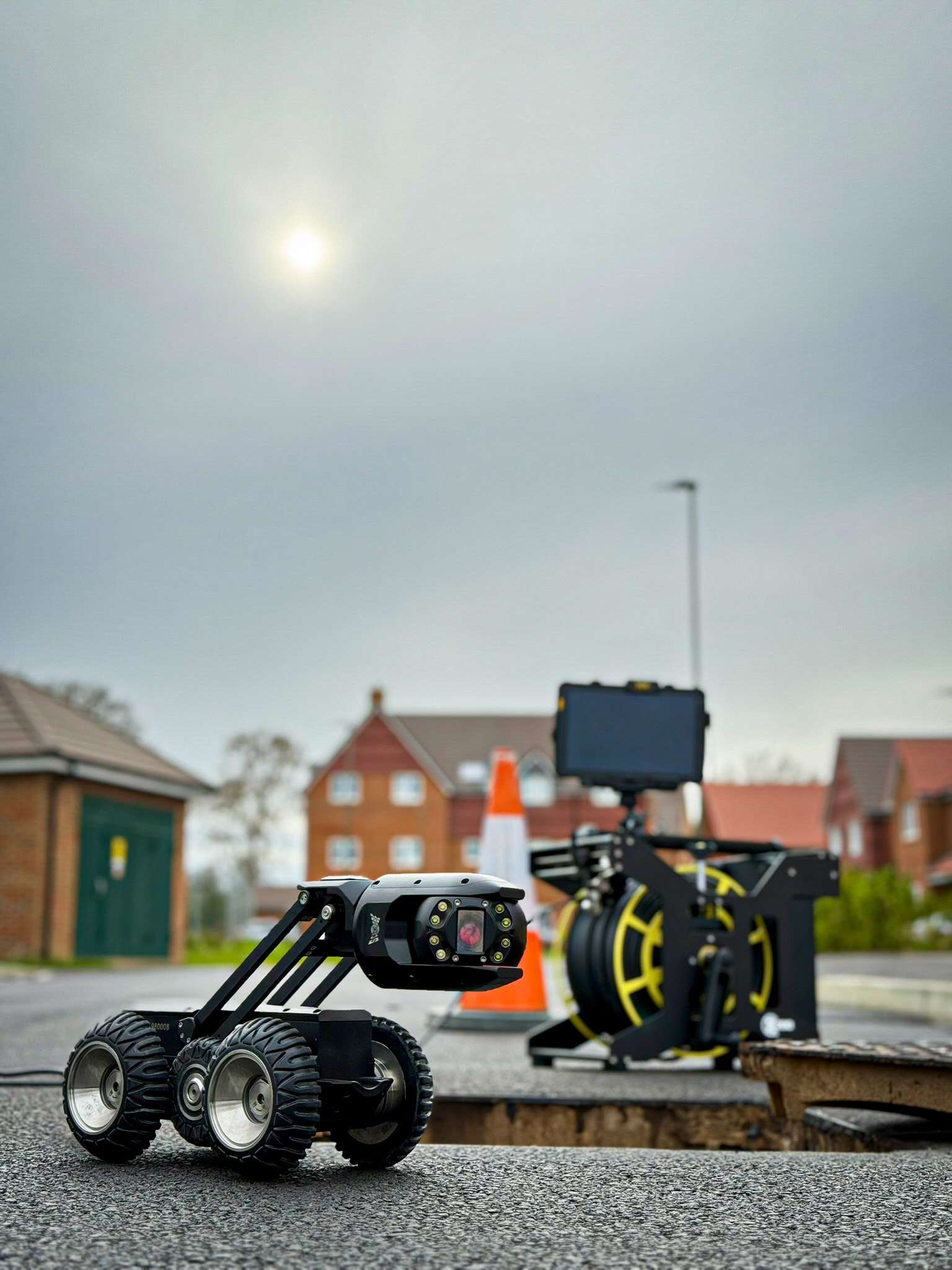 Scanprobe Maxius inspection crawler beside an open manhole, with its cable reel and control tablet in the background.
